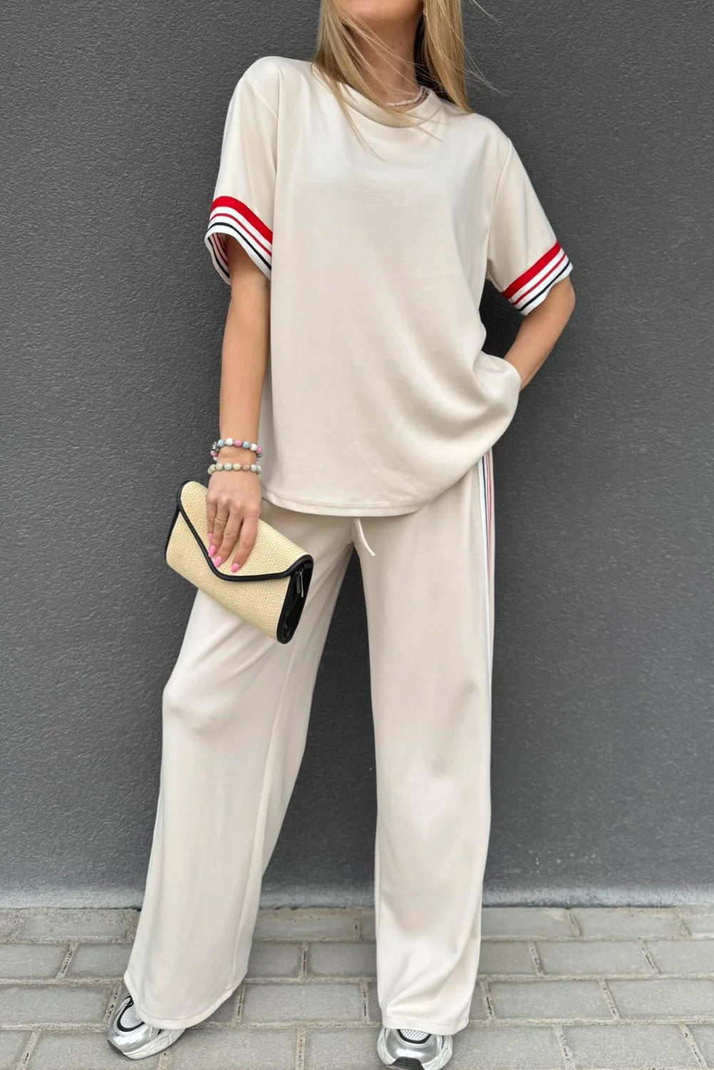 Person wearing a beige outfit with red and white striped sleeves against a gray wall.