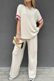 Person wearing a beige outfit with red and white striped sleeves against a gray wall.