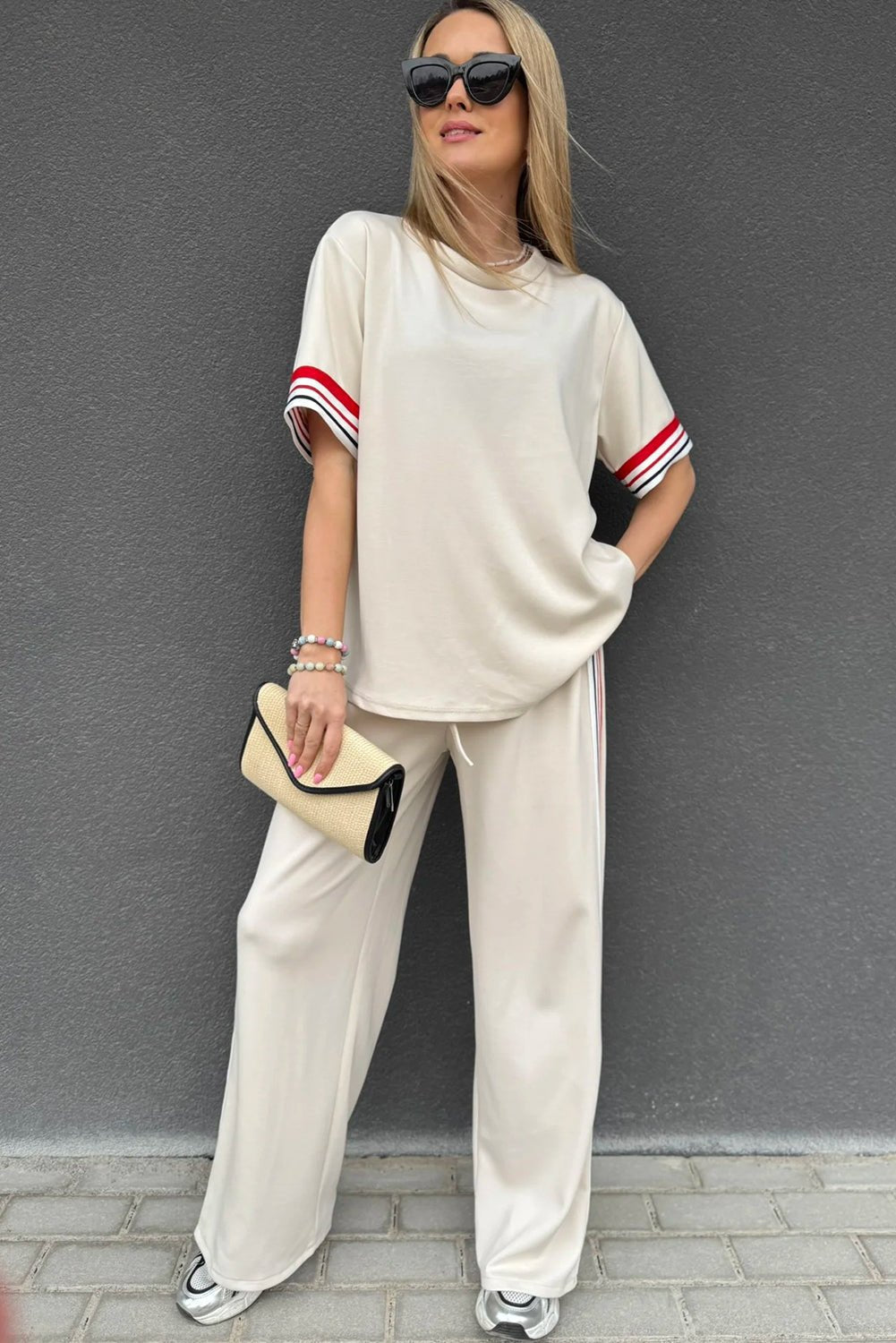 Woman wearing a beige outfit with red and black accents against a gray wall.