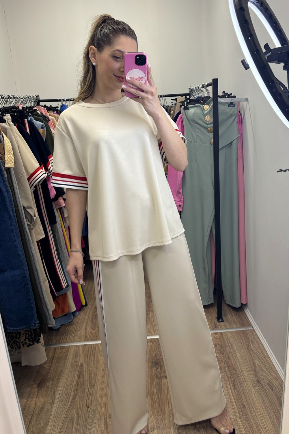 Woman taking a mirror selfie wearing a beige outfit in a clothing store.