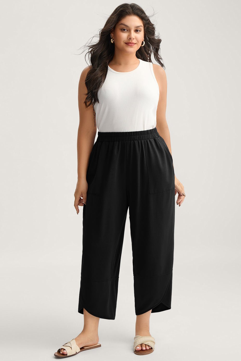 Woman wearing a white sleeveless top and black wide-leg pants on a plain background