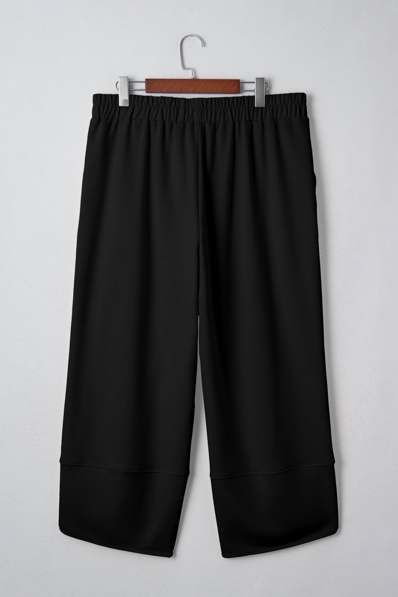 Black pants hanging on a wooden hanger against a white background
