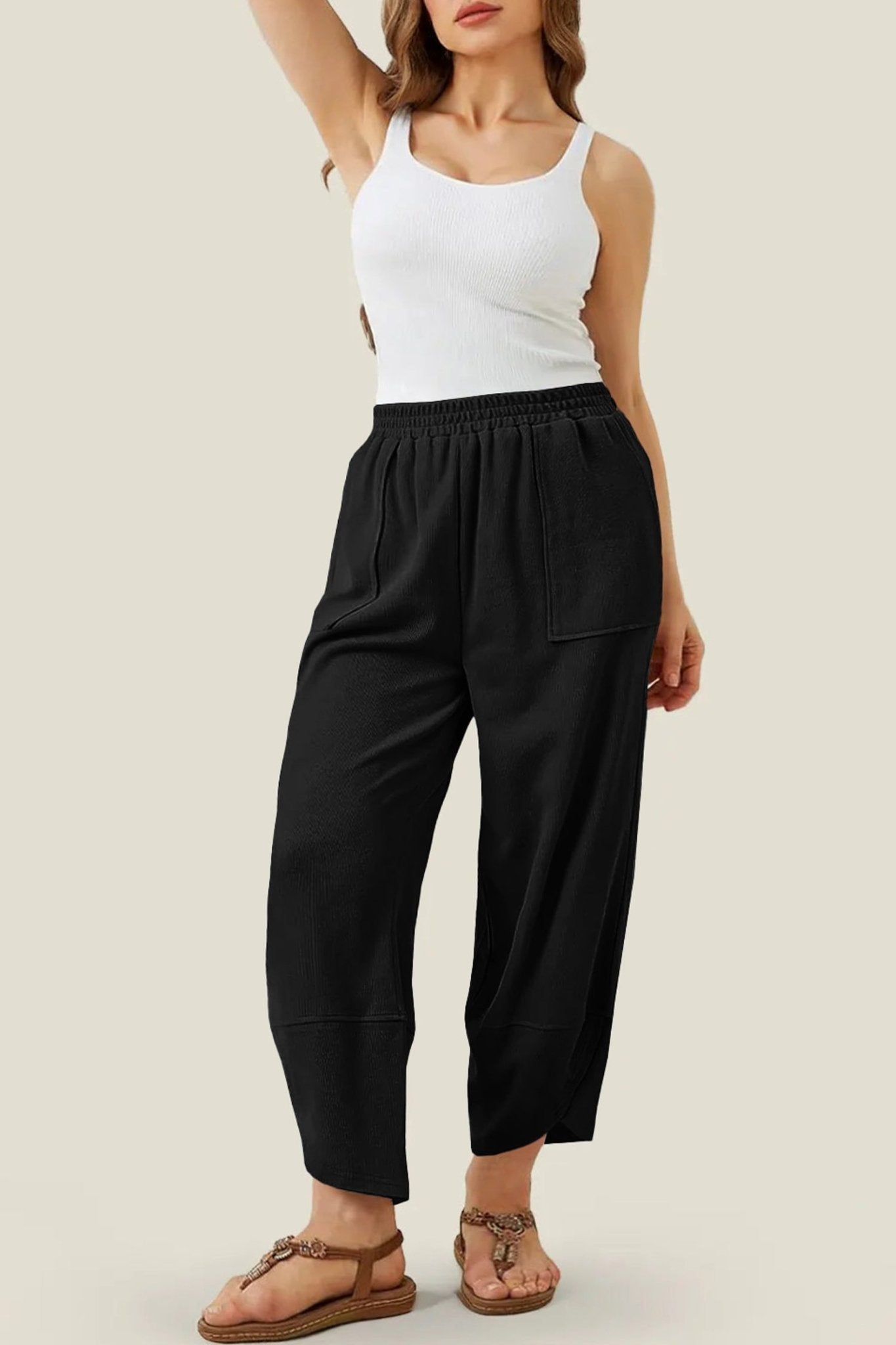 Woman wearing a white tank top and black high-waisted pants on a beige background
