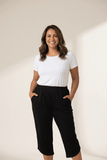 Woman wearing a white t-shirt and black capri pants against a plain background