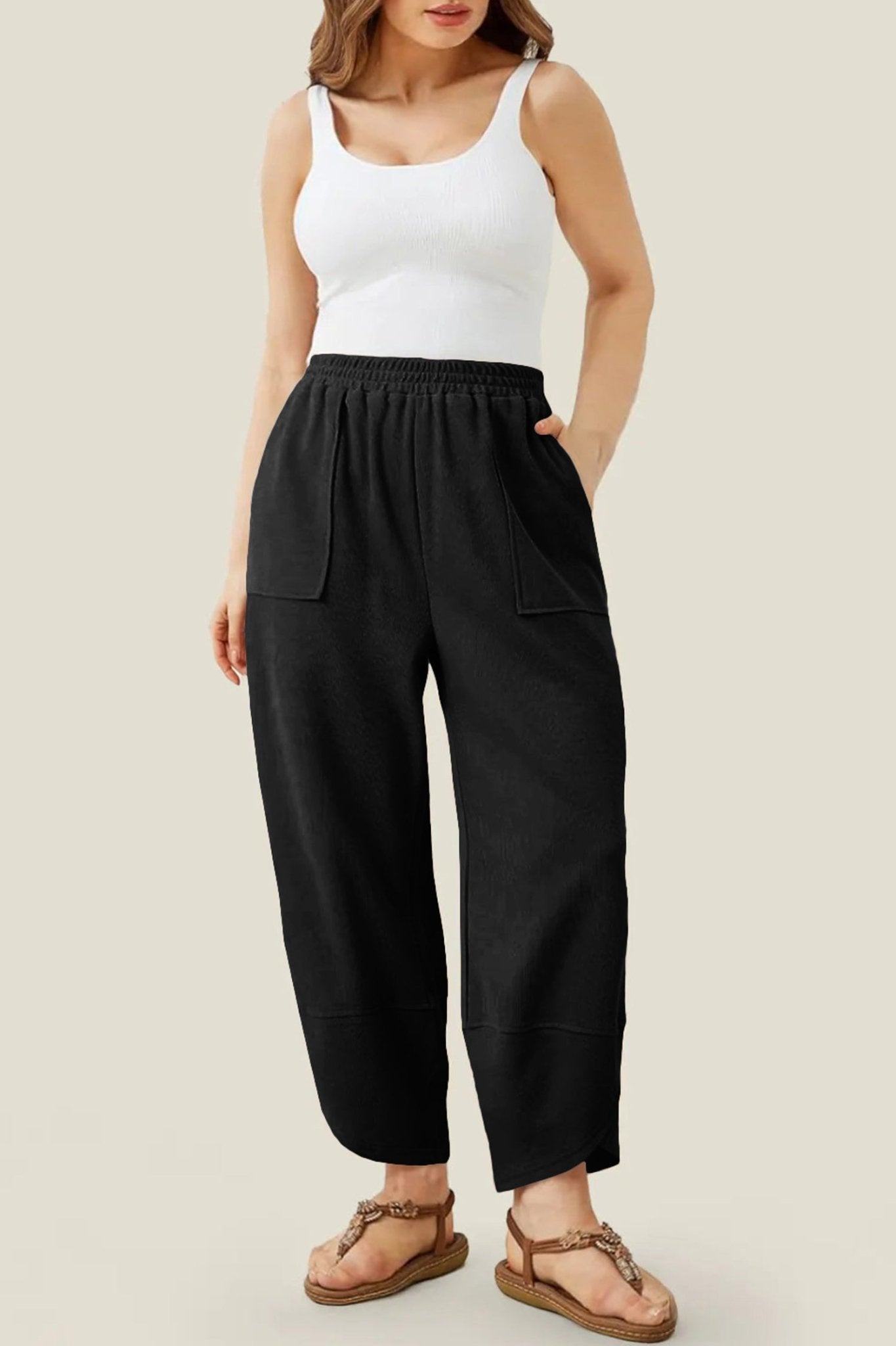 Person wearing black pants and a white tank top on a plain background