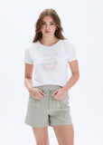 Woman wearing a white t-shirt with a graphic design and light gray shorts on a white background