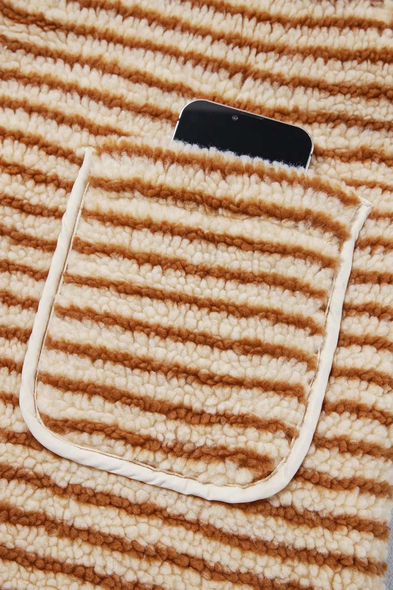 Close-up of cream-brown striped plush fabric with pocket and black smartphone.