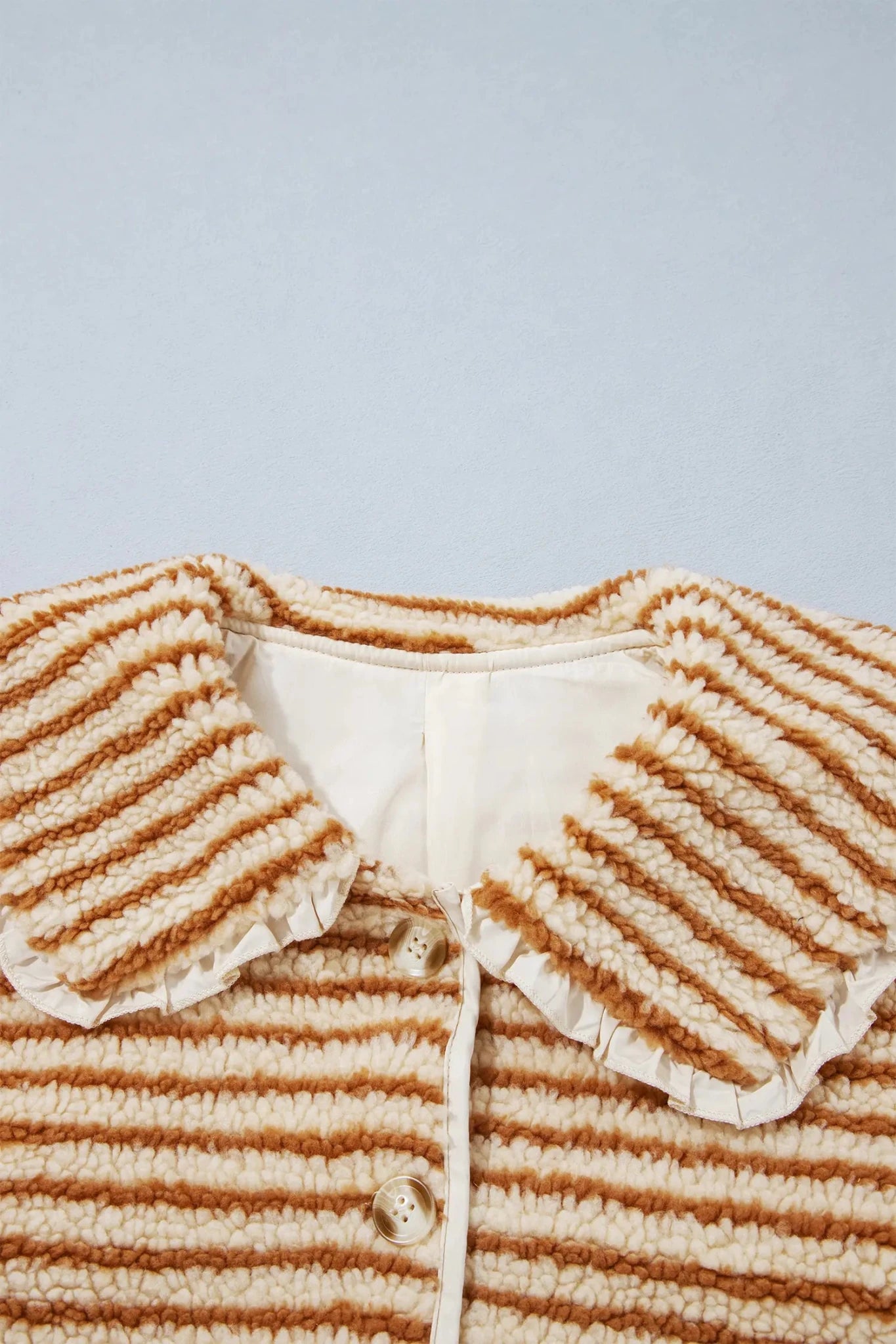 Close-up of brown-cream striped knit cardigan with ruffled collar and gold buttons.