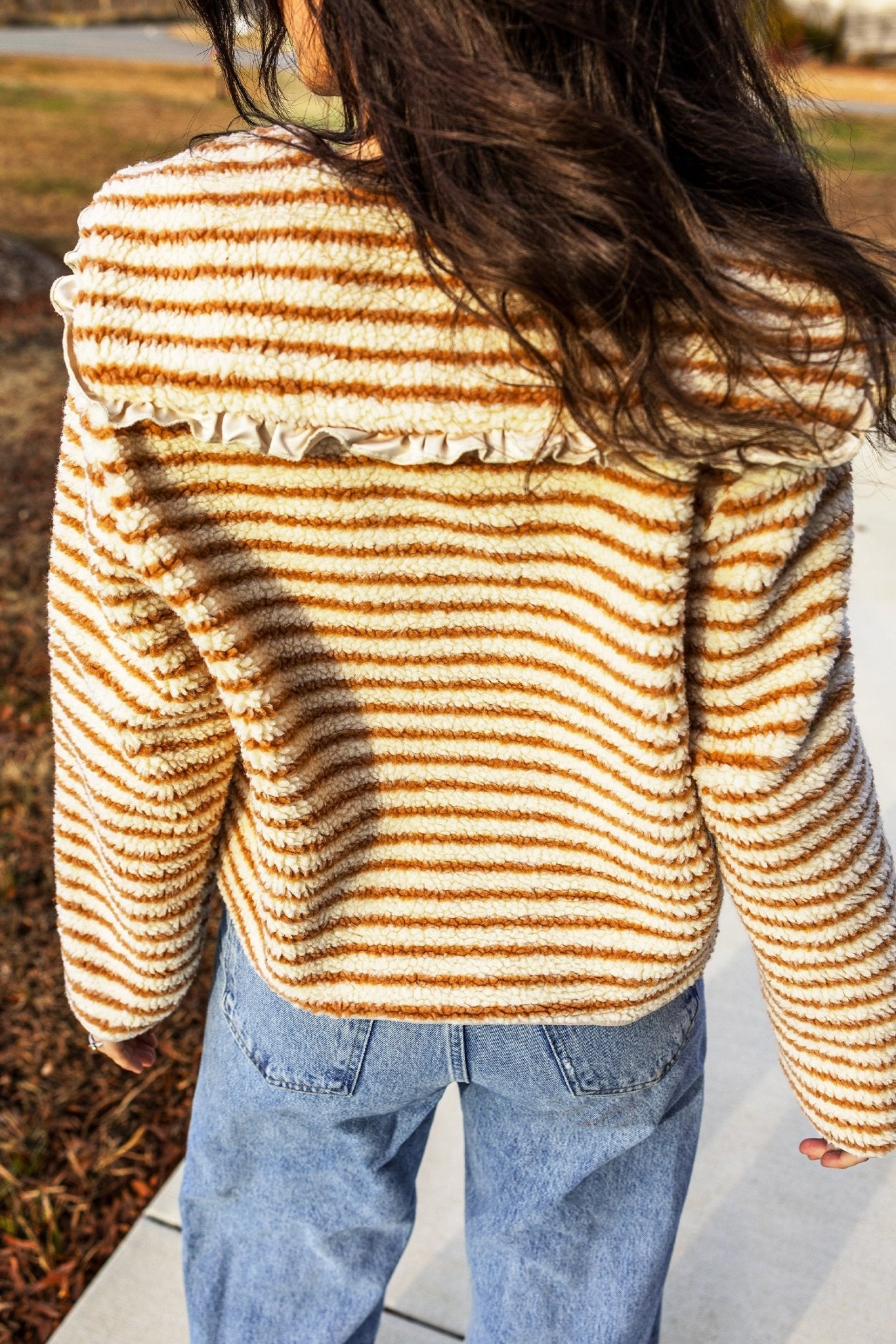 Back view of person in fuzzy striped sweater with ruffled collar and light jeans.