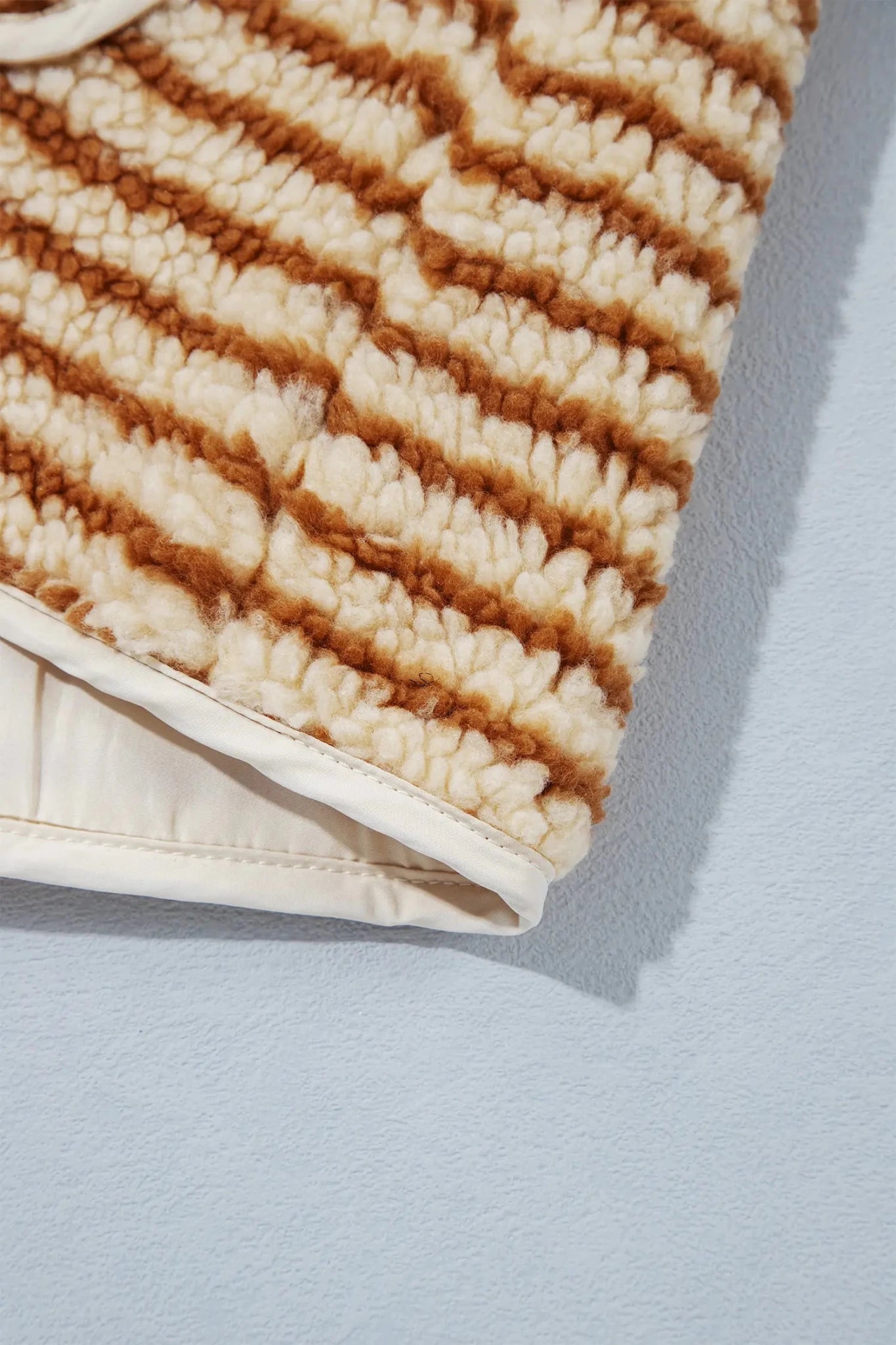Close-up of cream-brown striped fleece blanket with smooth cream border.
