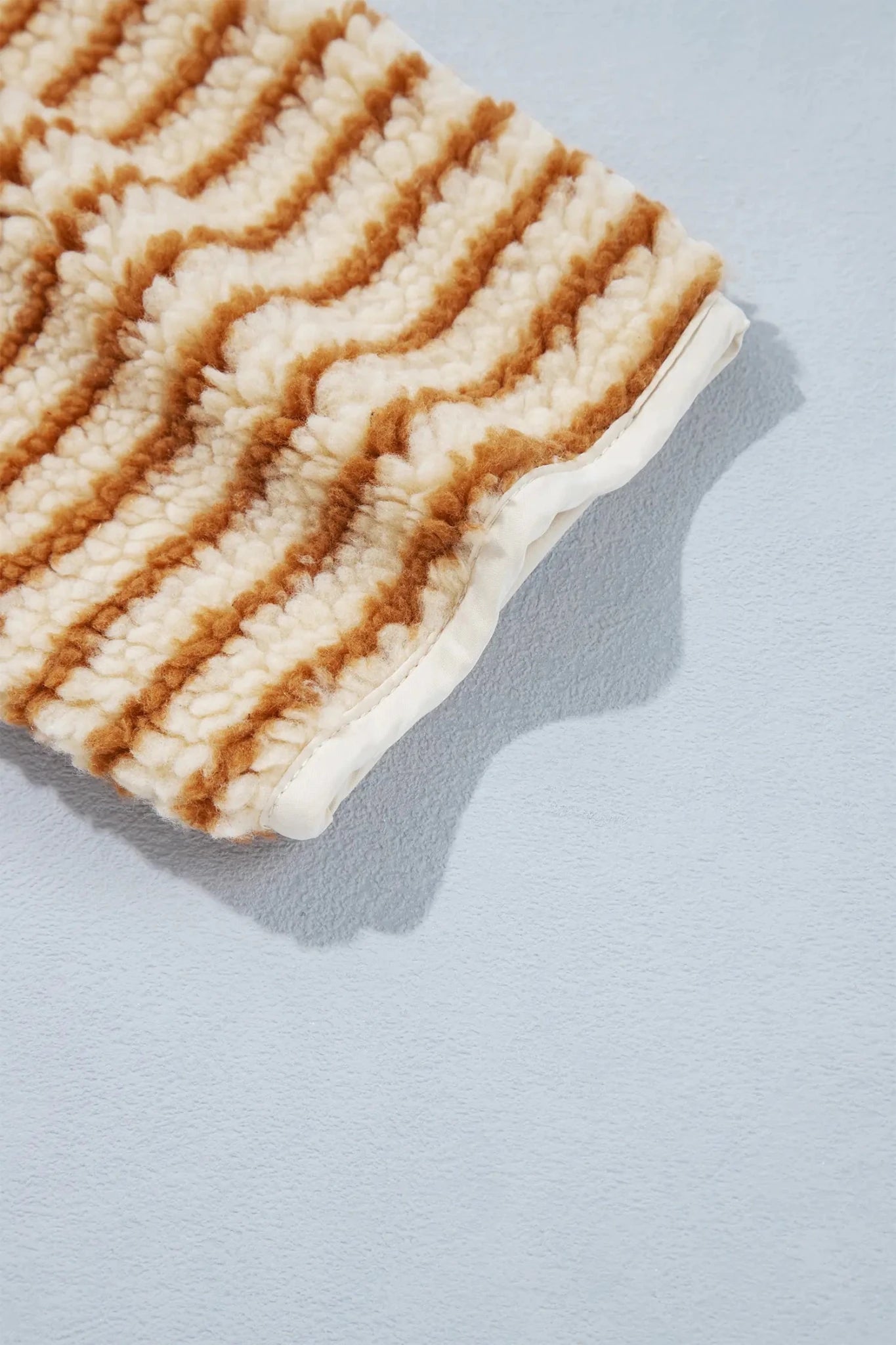 Close-up of cream-brown striped ribbed knit sleeve on a light blue-gray background.