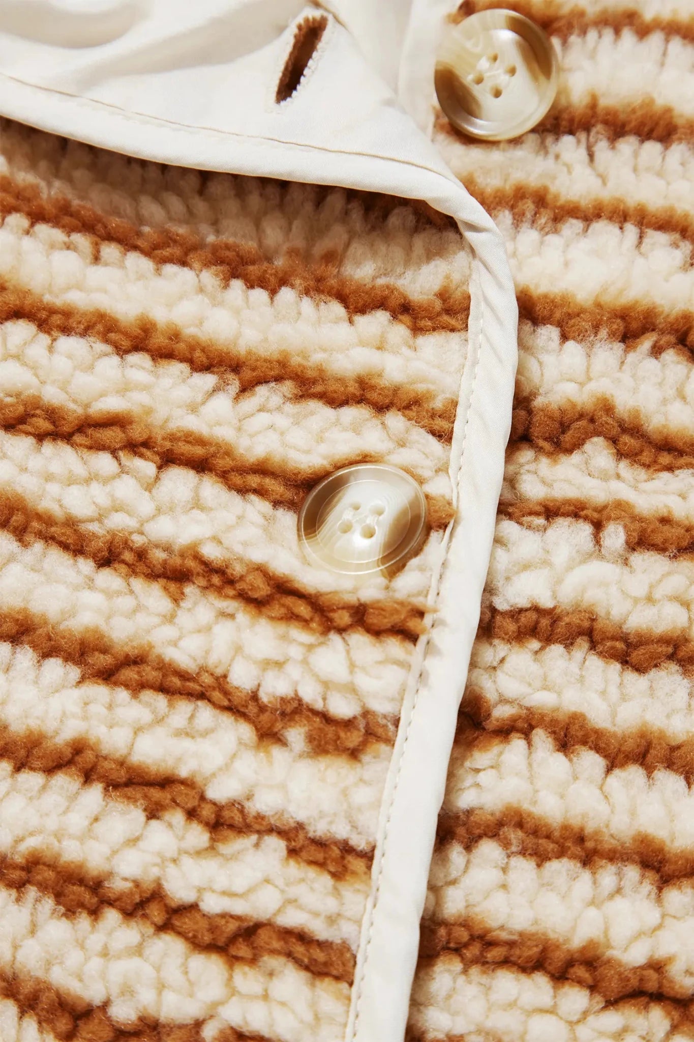 Close-up of brown-cream striped sherpa jacket with cream collar and amber buttons.