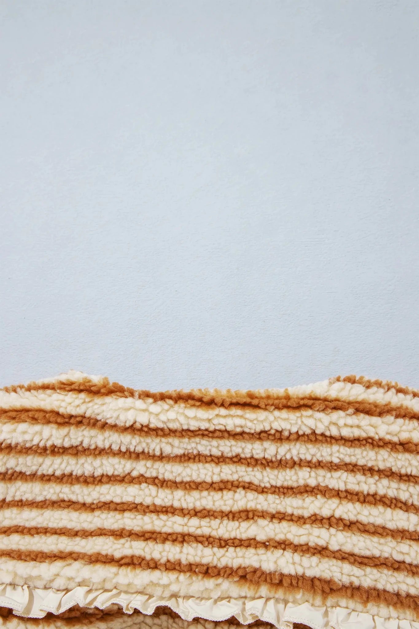 Close-up of cream and warm tan striped woven rug with ruffled edge.