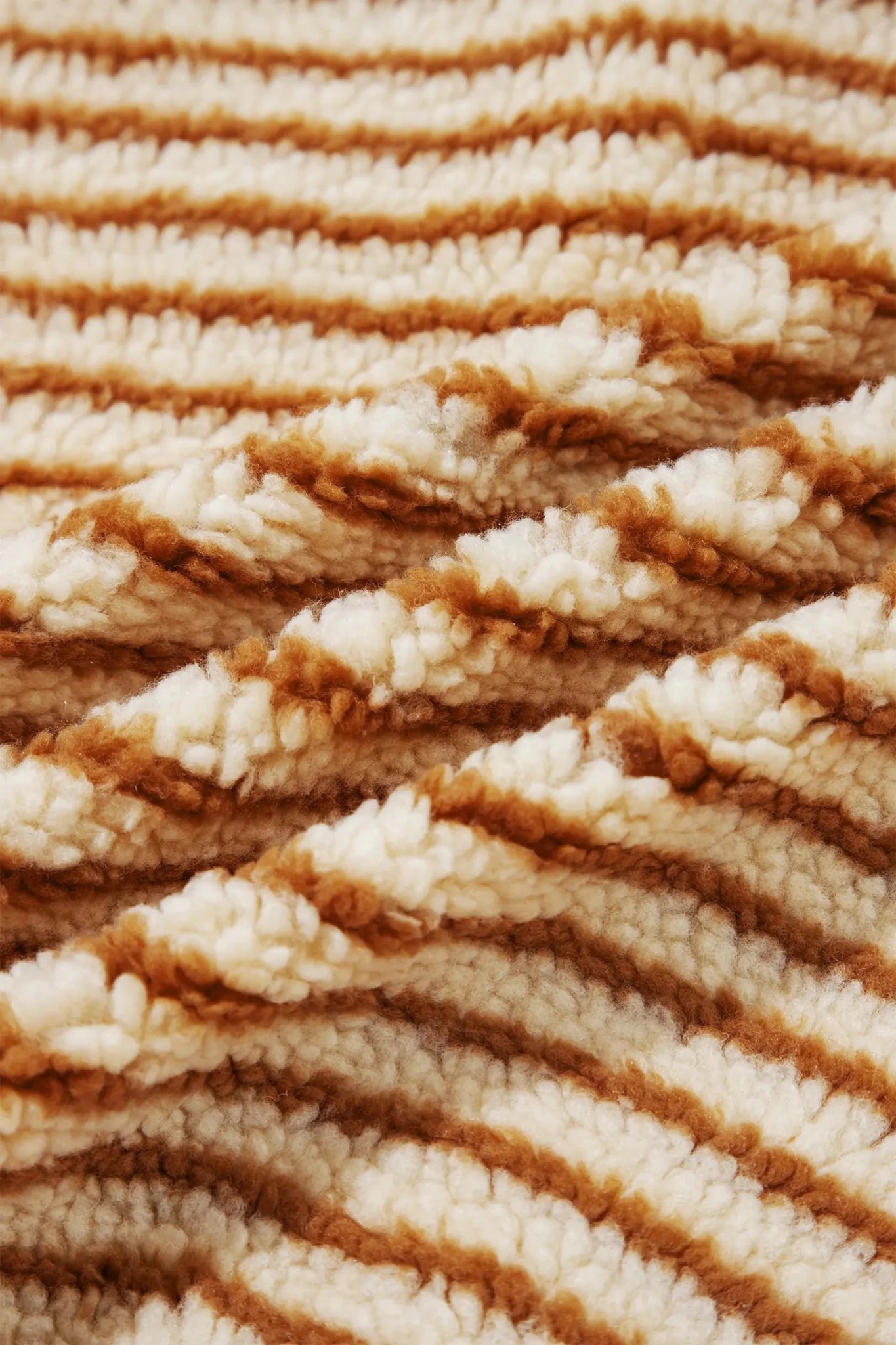 A close-up of a plush, textured striped fabric with alternating thick bands of cream and warm brown.