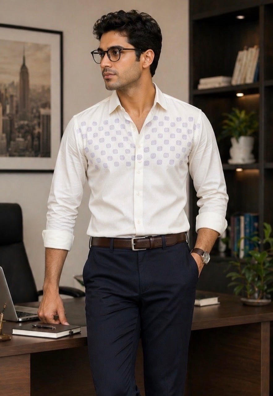 Man in a white patterned shirt and dark pants standing in an office setting.