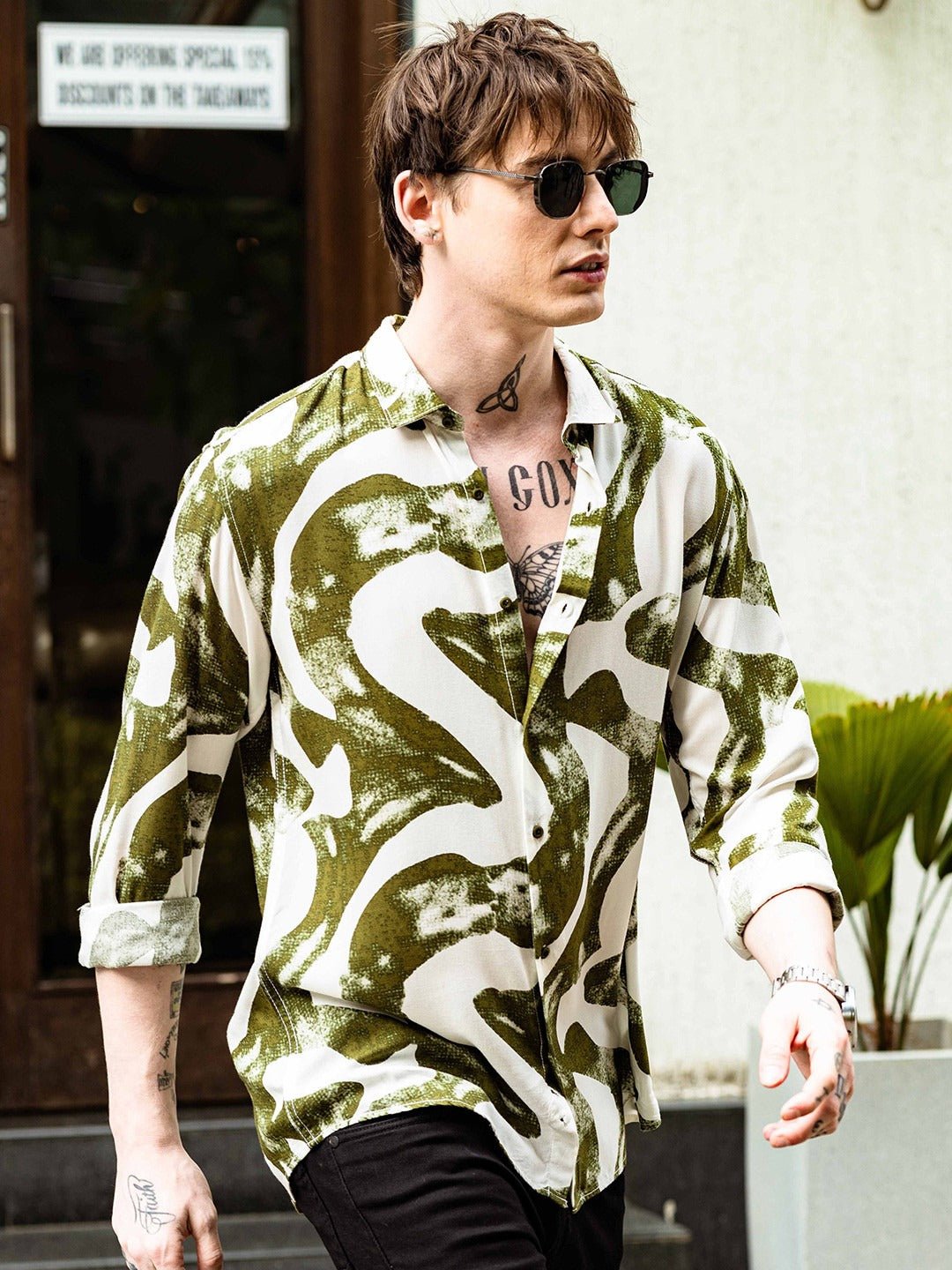 Person wearing a green and white patterned shirt with tattoos visible on arms and neck.