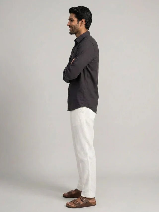 Man wearing a dark shirt and white pants standing against a plain background