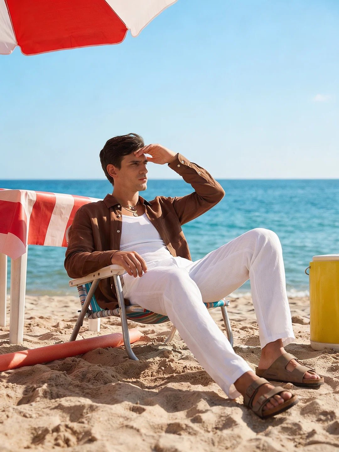 Man sitting on a beach chair under an umbrella with ocean in the background