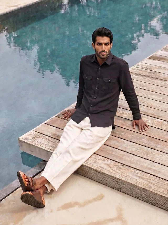 Man sitting by a pool wearing a black shirt and white pants.