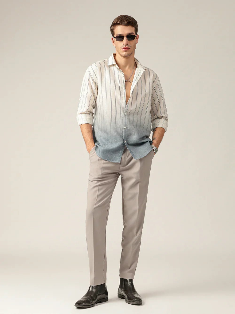 Man wearing a striped shirt, light gray pants, and dark shoes on a plain background