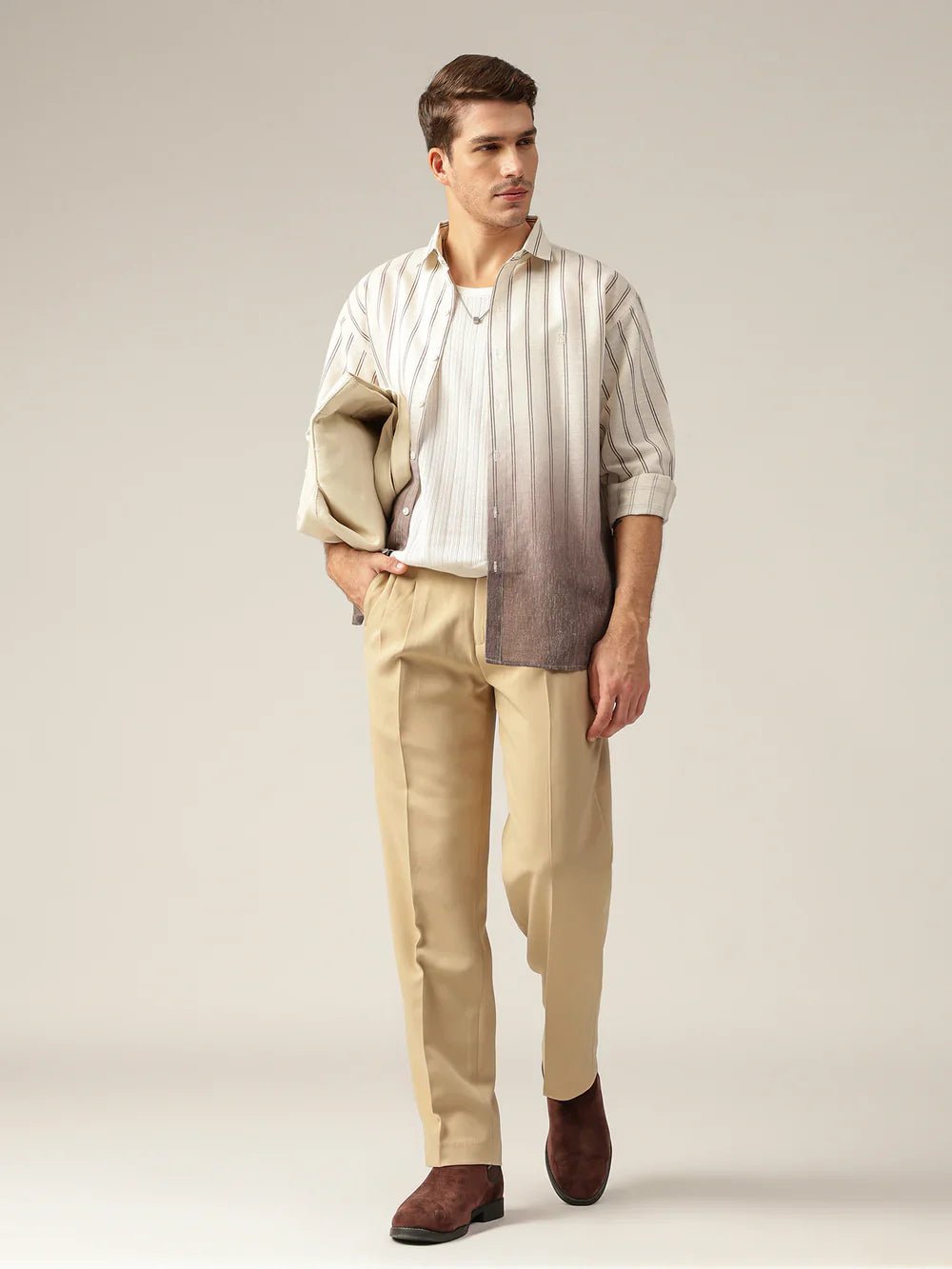 Man wearing a striped shirt with a beige jacket and pants on a plain background