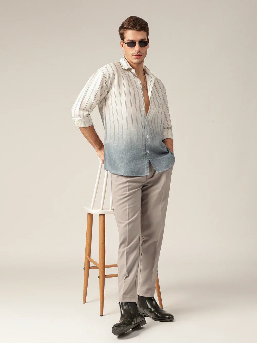 Man wearing a striped shirt with a gradient effect and beige pants, standing against a plain background.