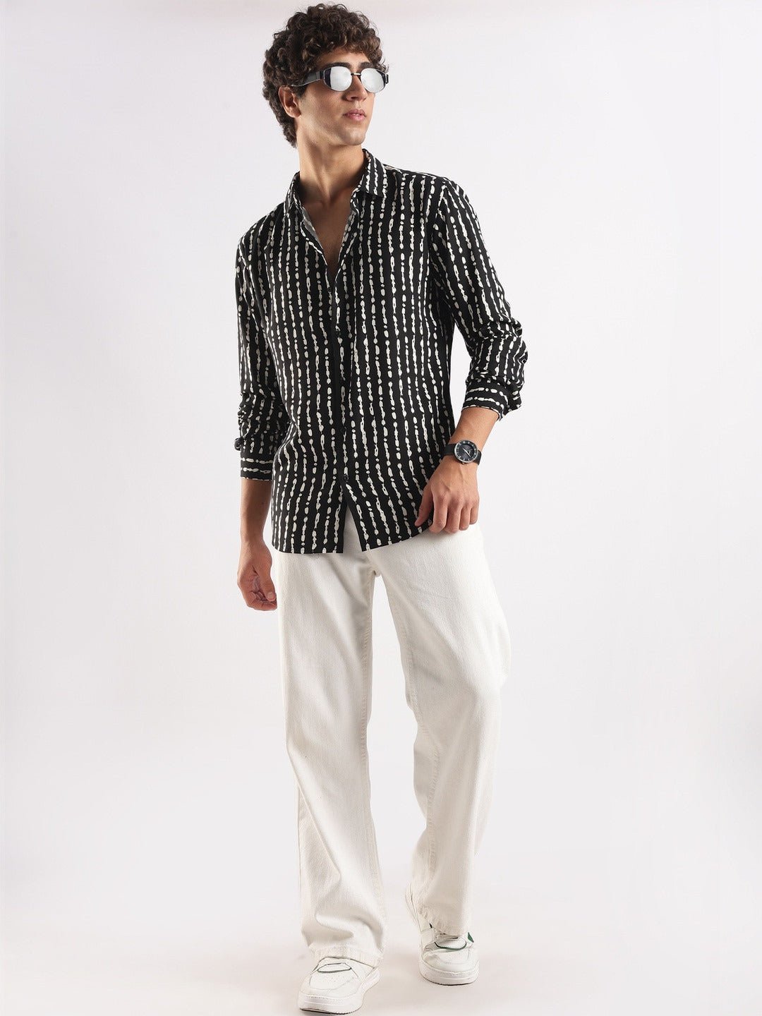 Man wearing a black and white patterned shirt with white pants on a white background