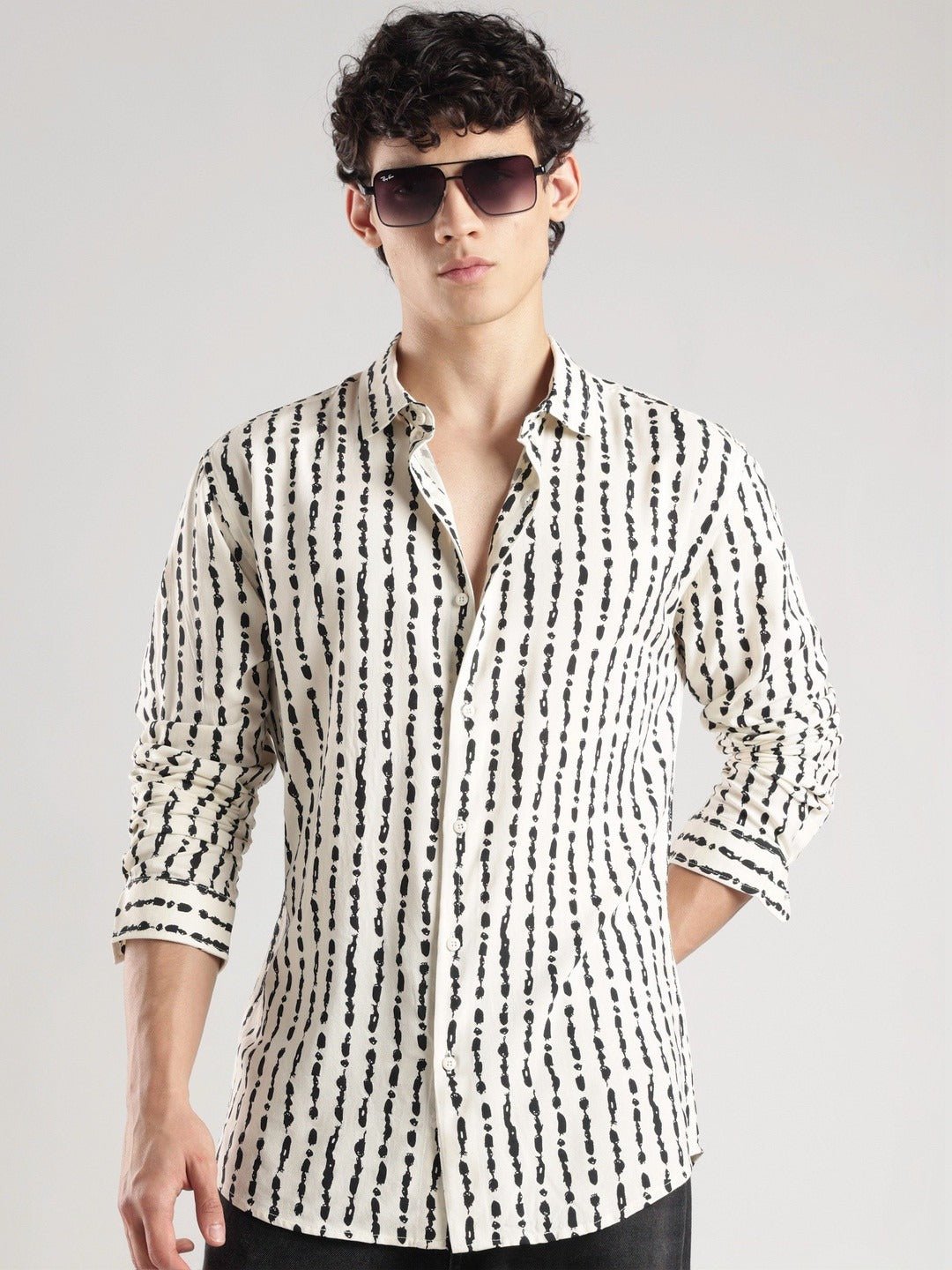 Man wearing a black and white patterned shirt with sunglasses on a gray background