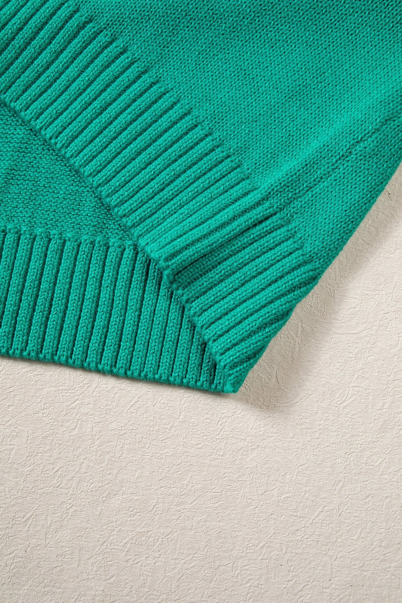 Close-up of teal-green ribbed knit fabric with V-shaped neckline or sleeve edge on a neutral background.