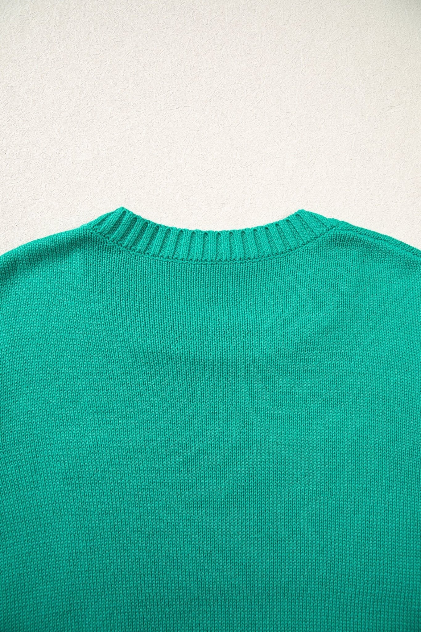 Close-up of the back of a bright green knit sweater against a plain off-white wall.