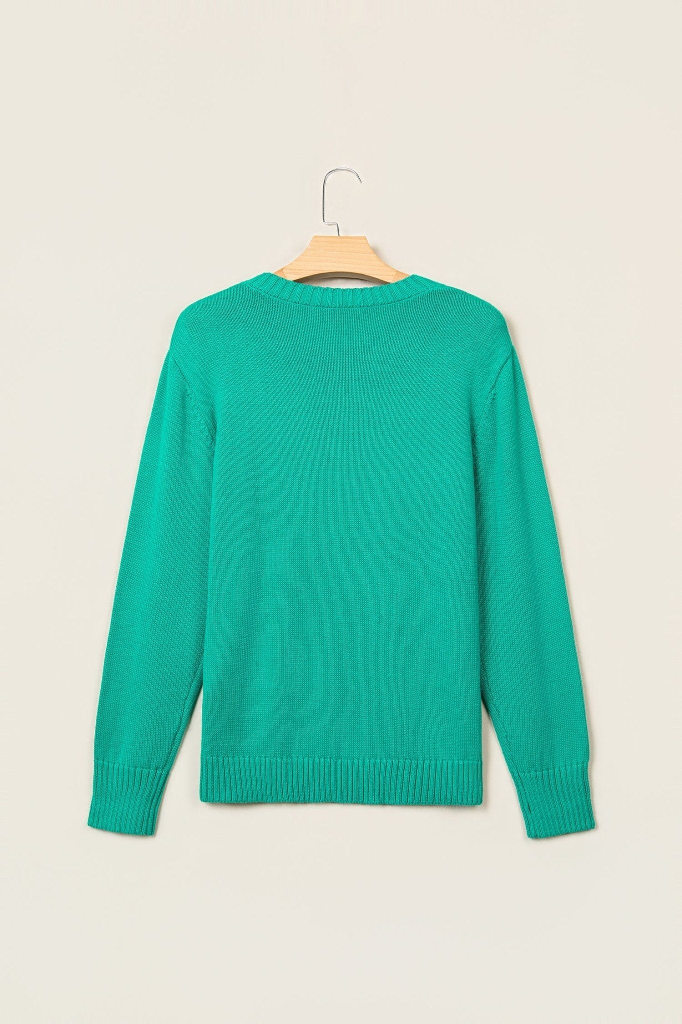 A bright green long-sleeve knit sweater hanging on a wooden hanger against a plain beige background.