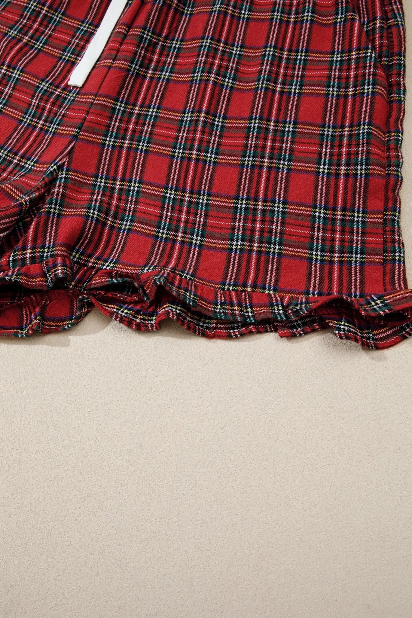 Close-up of red plaid shorts with ruffled hem and white drawstring.