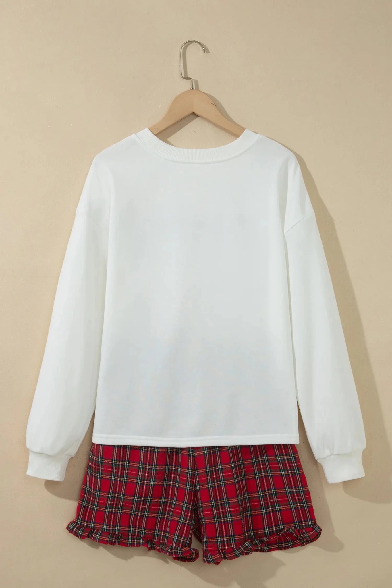 White crewneck sweatshirt with red-green plaid shorts on wooden hanger.