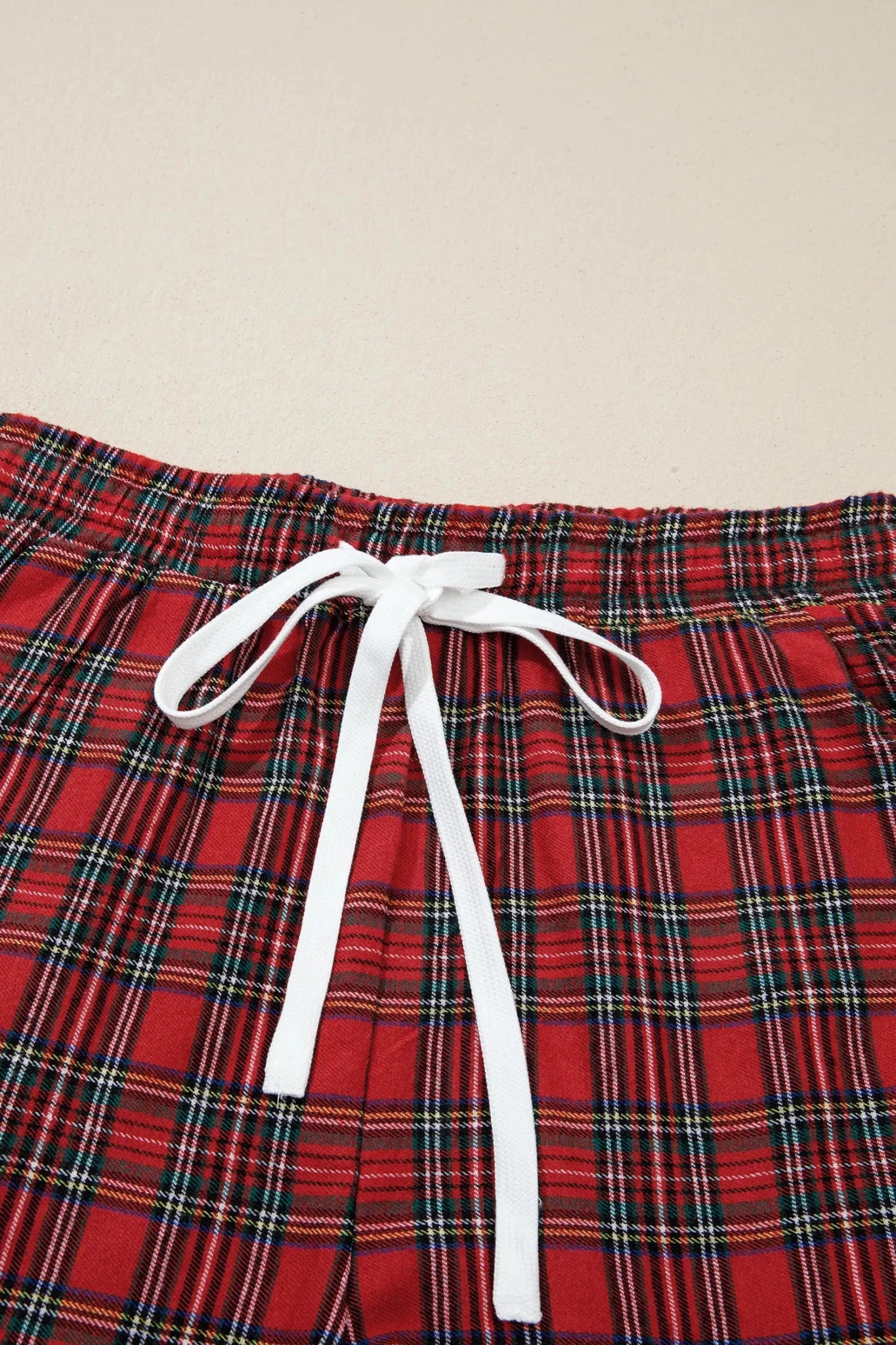 Close-up of red tartan plaid shorts with white drawstring.