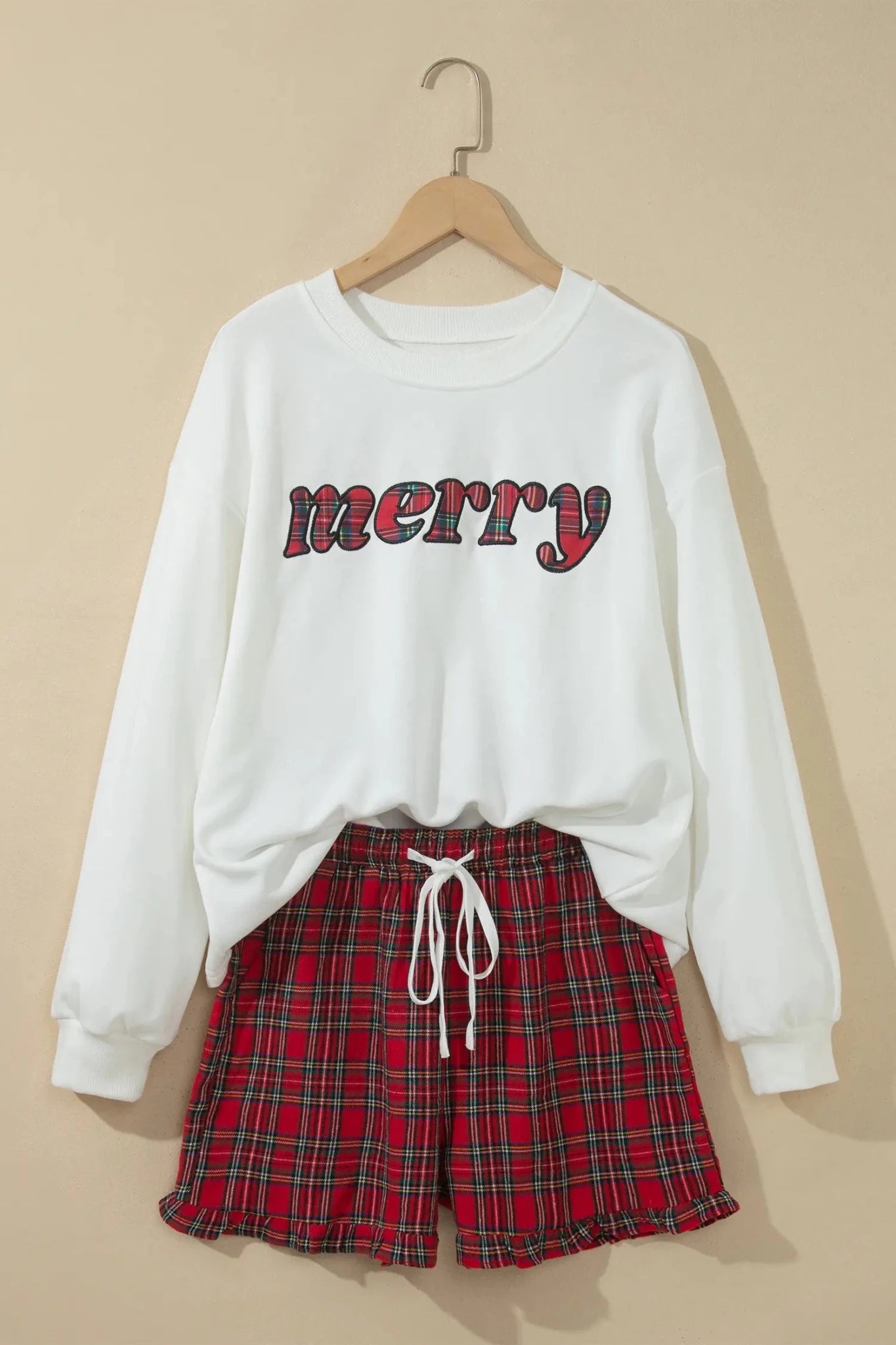White MERRY sweatshirt with red-black plaid shorts on wooden hanger.