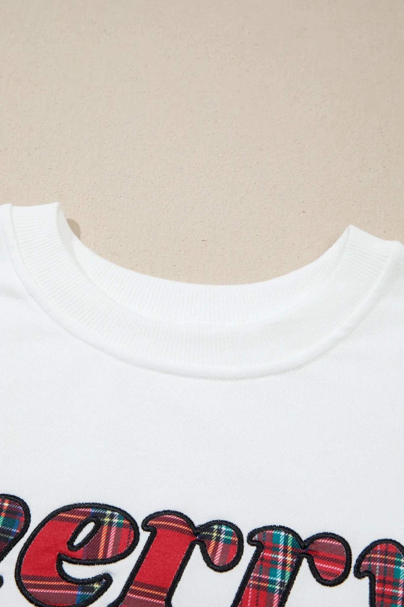 Close-up of white sweatshirt with red, green, and blue plaid graphic.