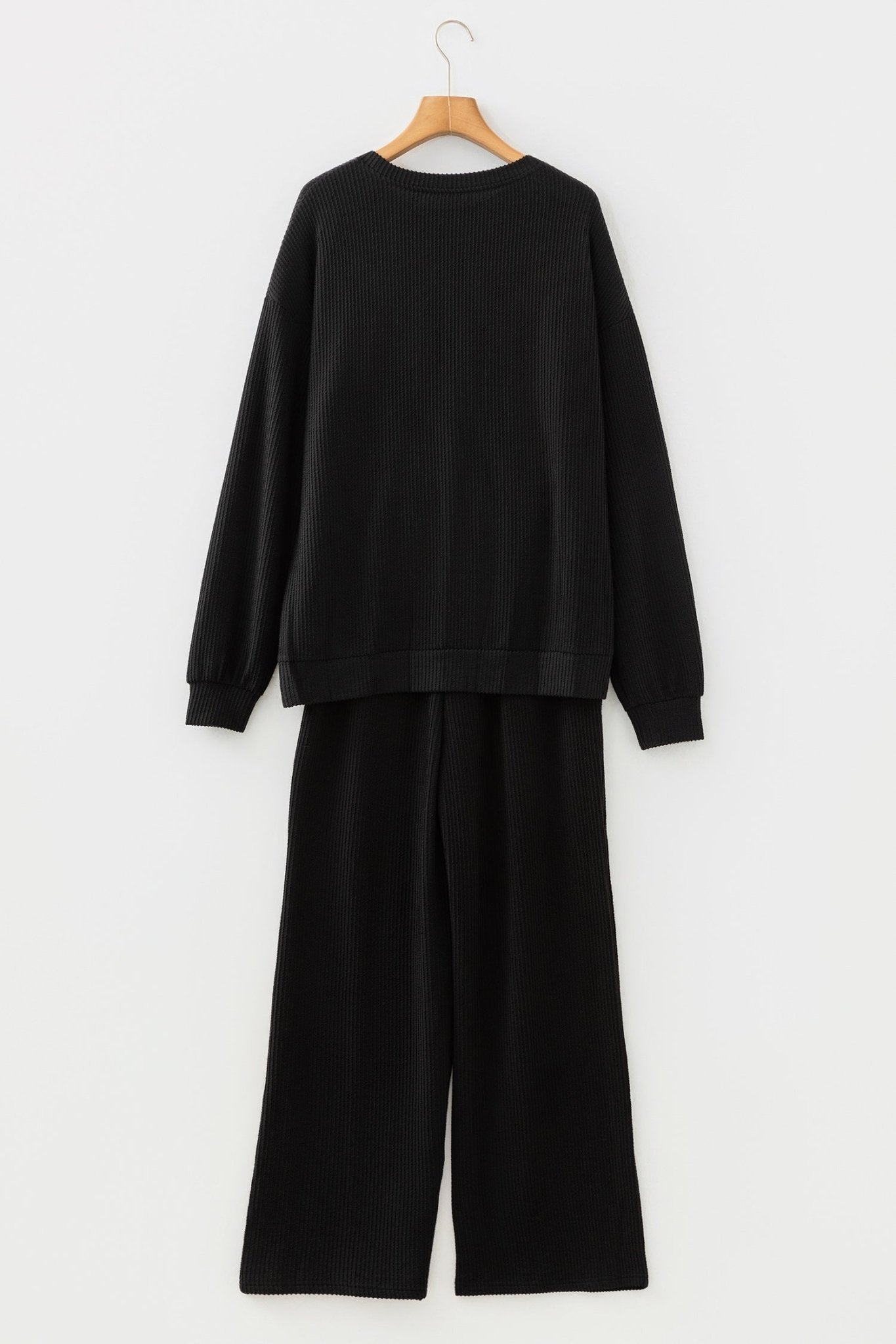Black sweatshirt and pants set on a hanger against a white background
