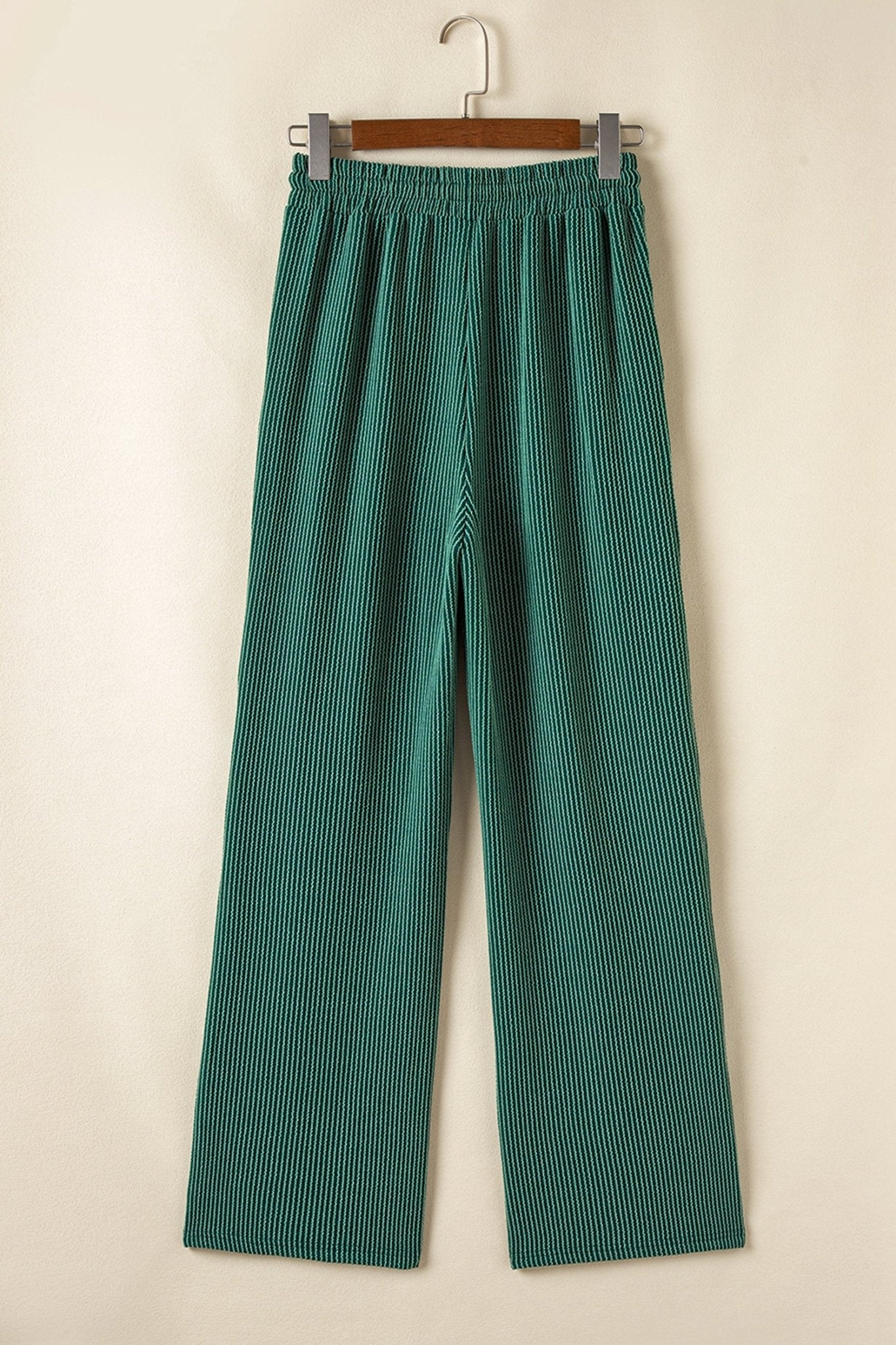 Green striped pants on a hanger against a beige background