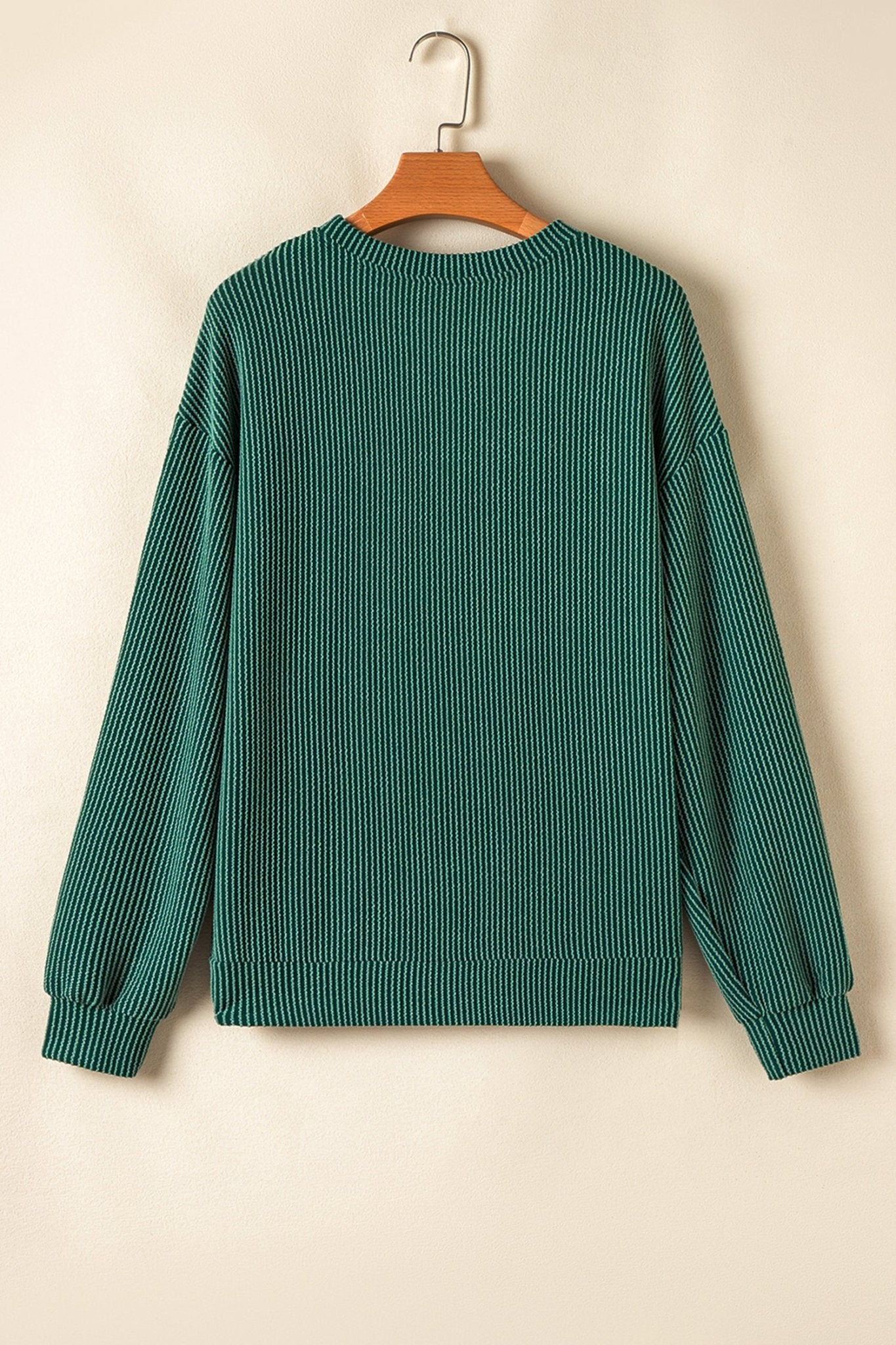 Green ribbed sweater on a wooden hanger against a beige background
