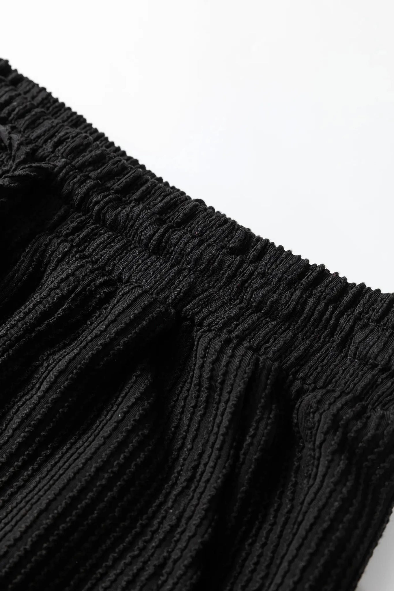 Black textured garment with gathered elastic waistband and ribbed fabric.