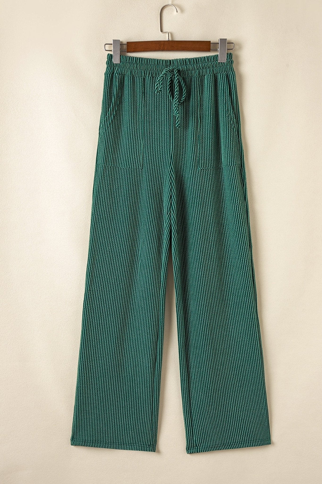 Green striped pants hanging on a wooden hanger against a beige background