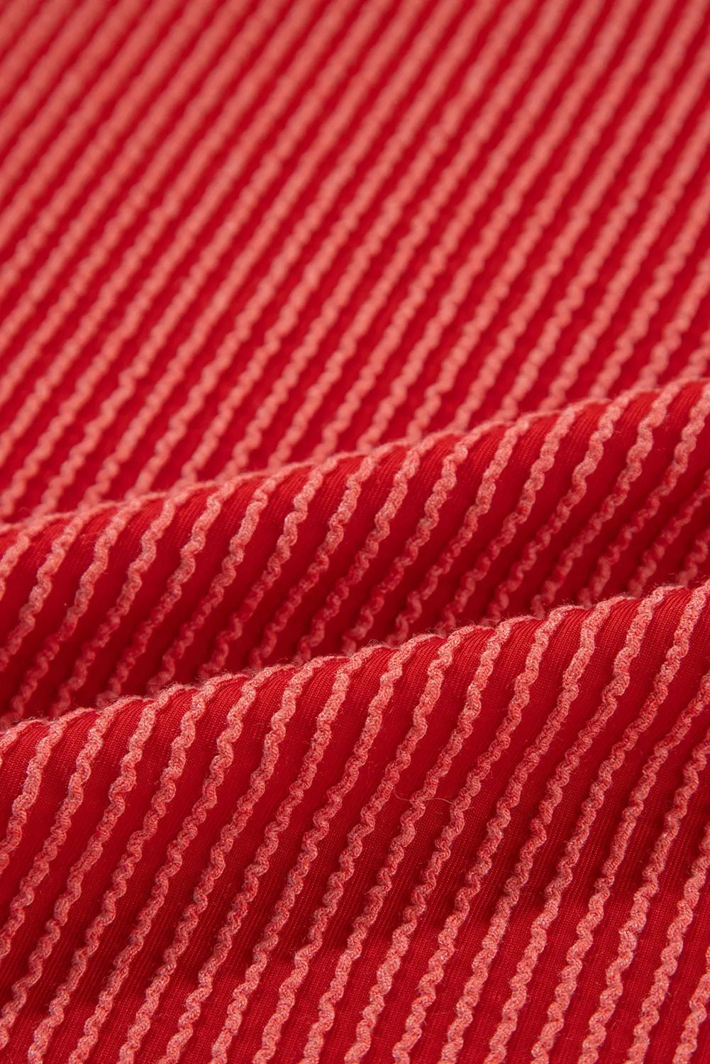 A close-up of red fabric with thin, evenly spaced light pink stripes running diagonally across the surface.