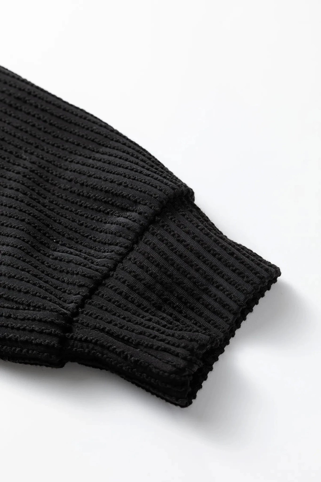 Close-up of a black ribbed sweater sleeve on a white background