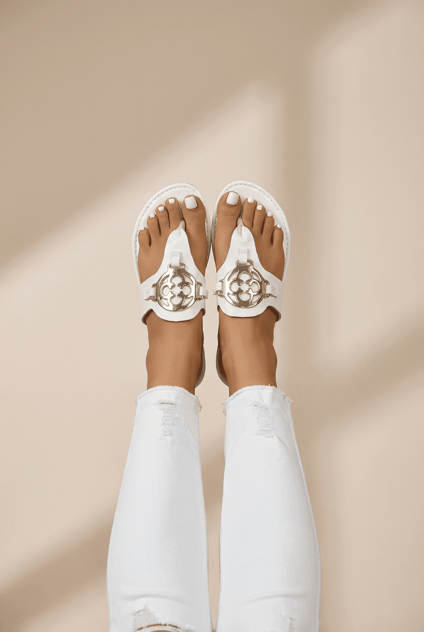 White sandals with gold embellishments worn on a beige background