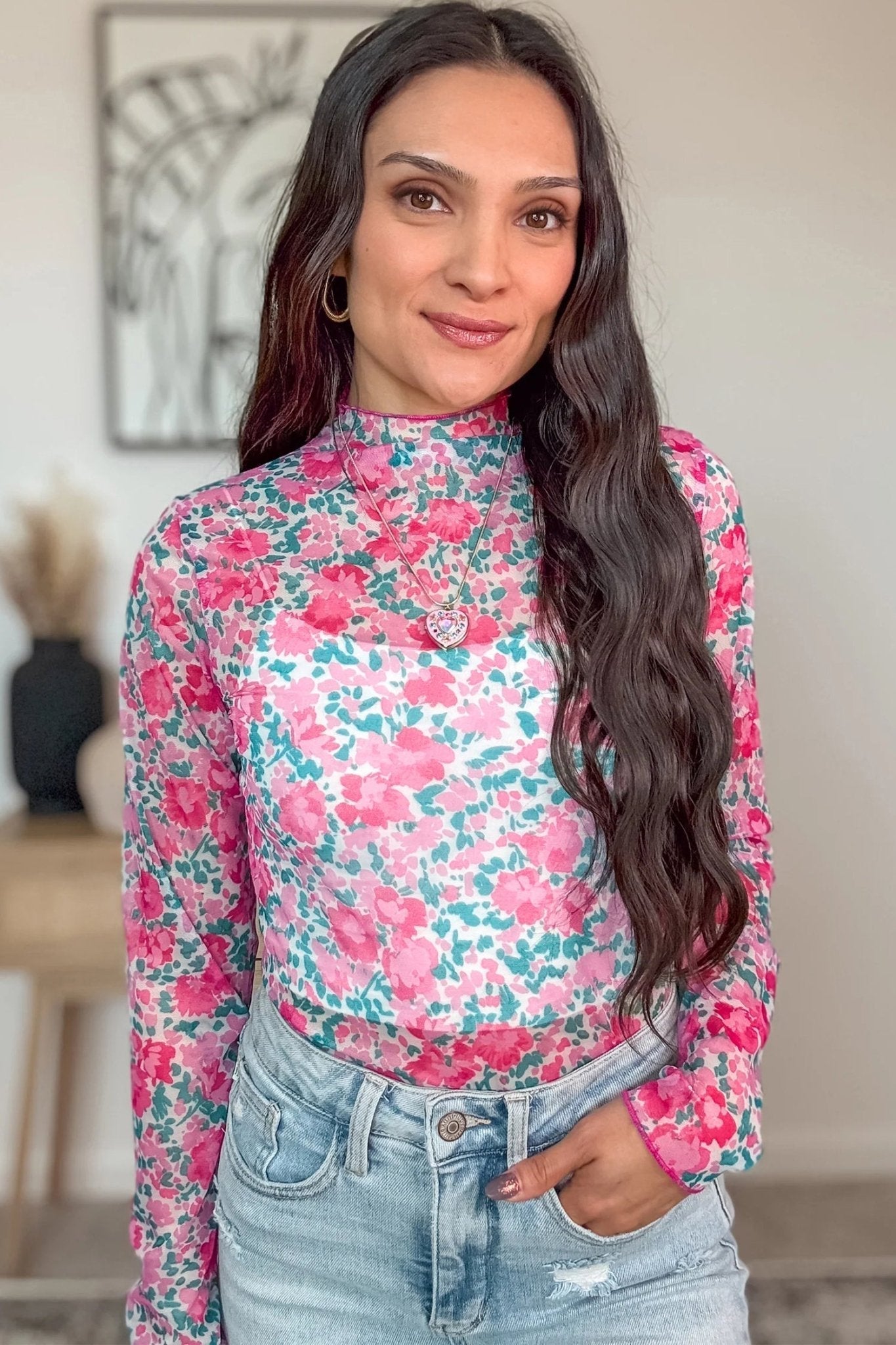 Woman wearing a floral long-sleeve top and jeans indoors.
