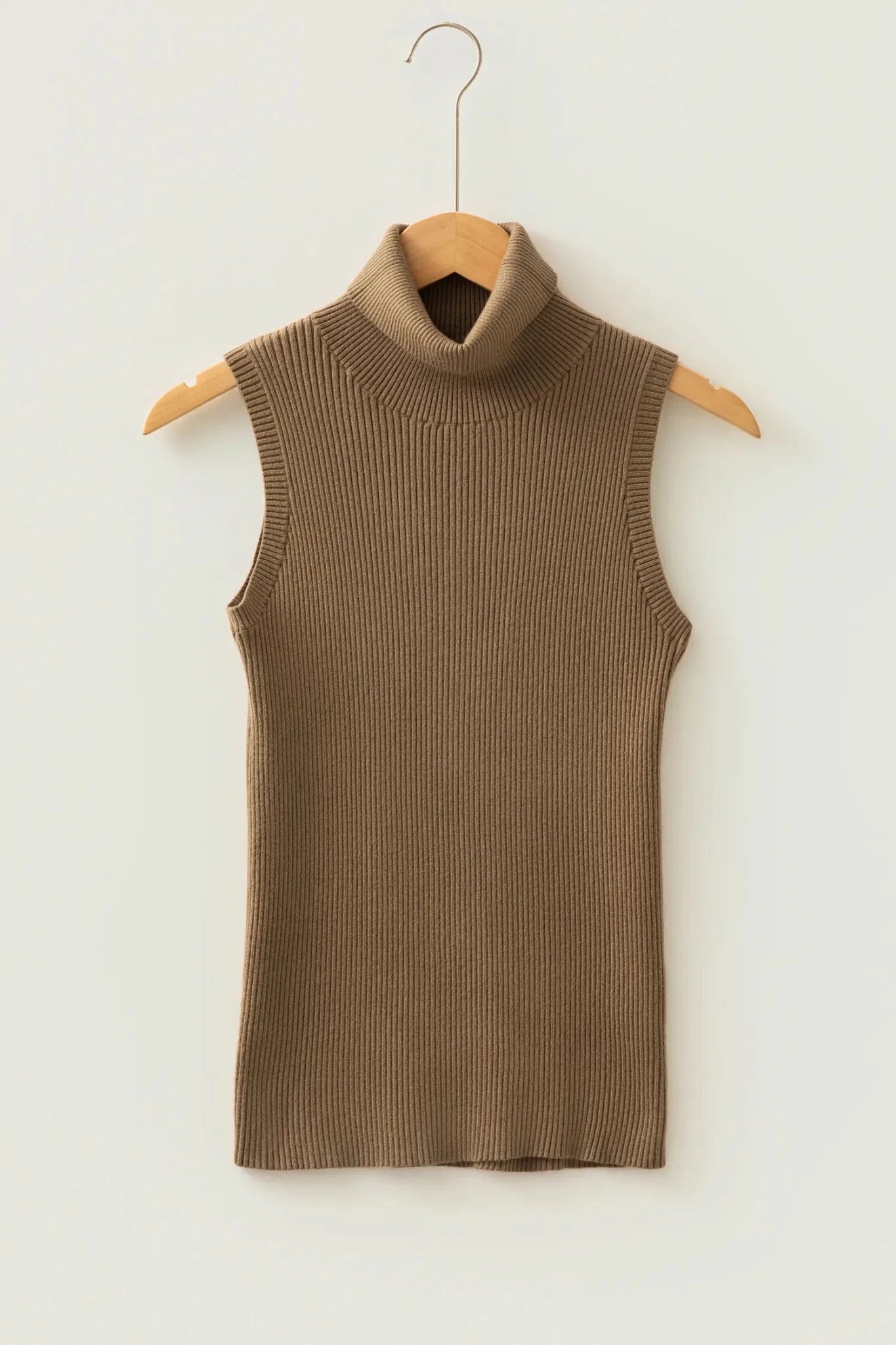 Taupe ribbed knit turtleneck sweater vest hanging on a wooden hanger against an off-white wall.