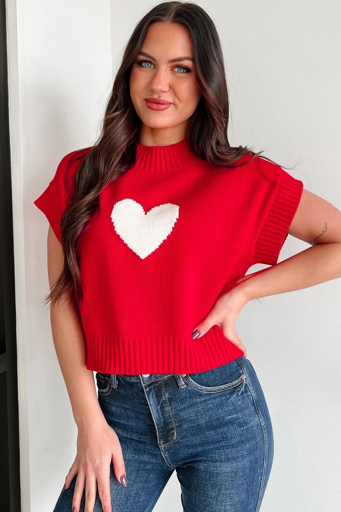 Woman wearing a red sleeveless sweater with a white heart design against a white background