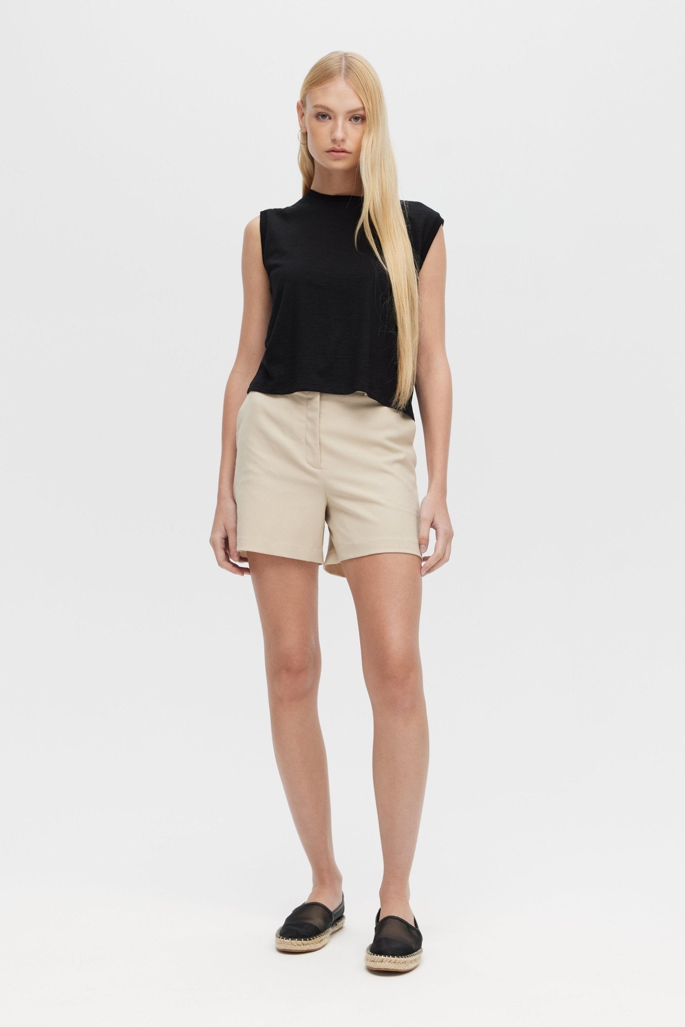 Woman wearing a black sleeveless top and beige shorts on a white background