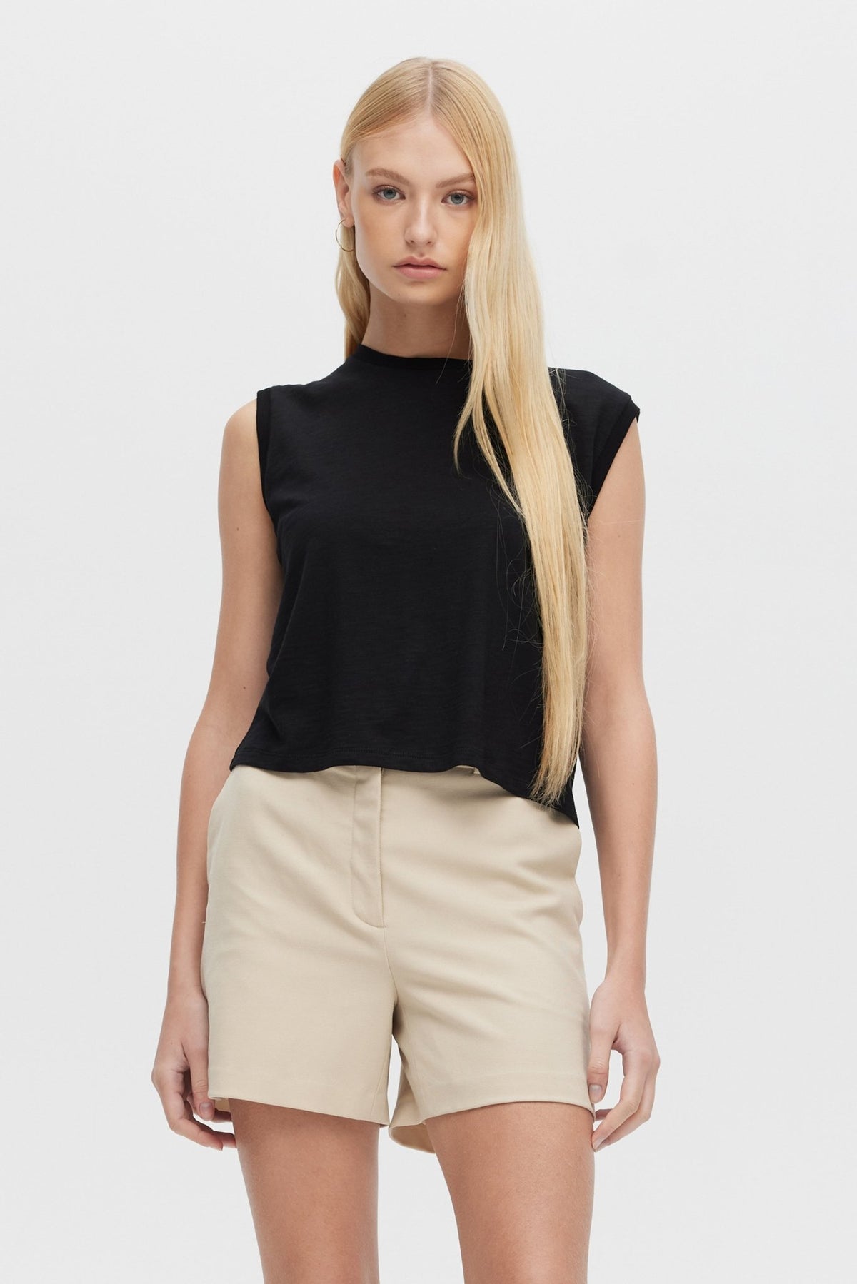 Woman wearing a black sleeveless top and beige shorts on a white background
