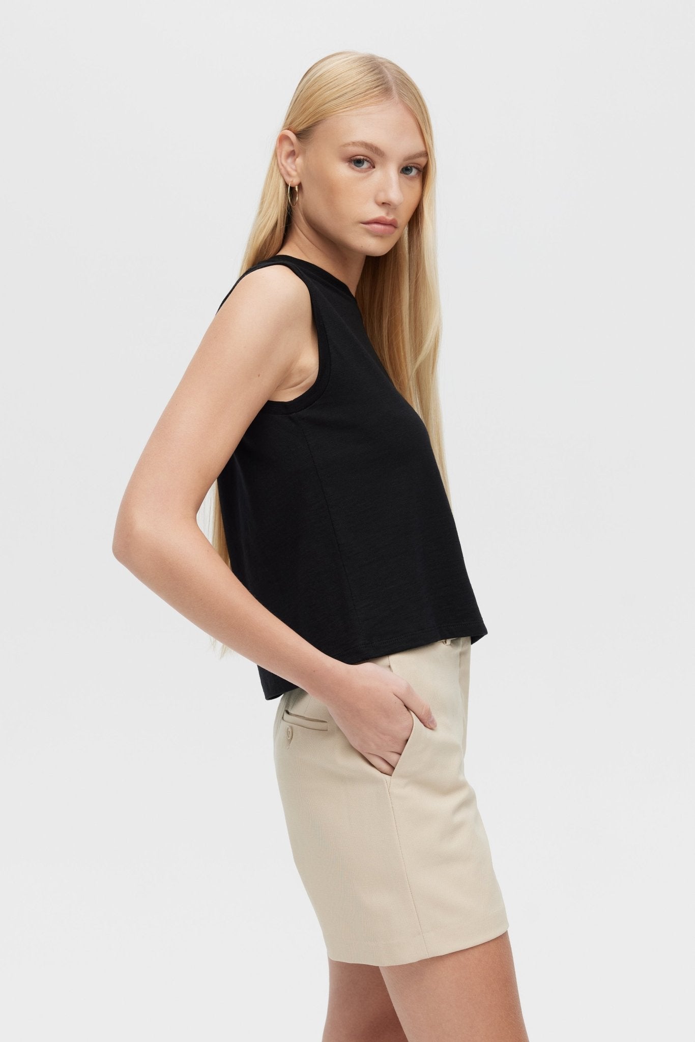 Woman wearing a black sleeveless top and beige shorts on a white background